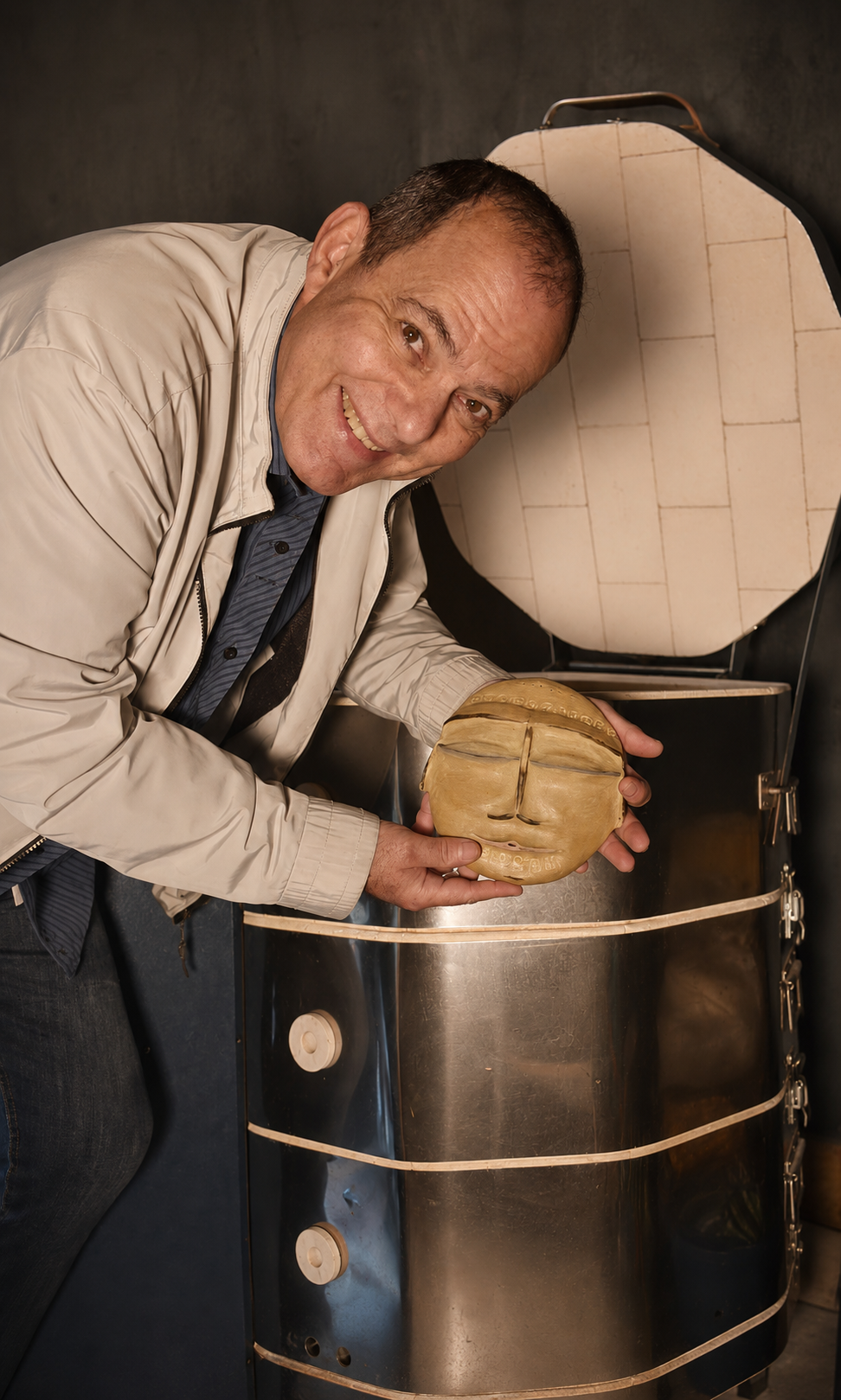 Fernando Lyra en su taller de cerámica, junto al horno, sosteniendo una obra de su autoría.